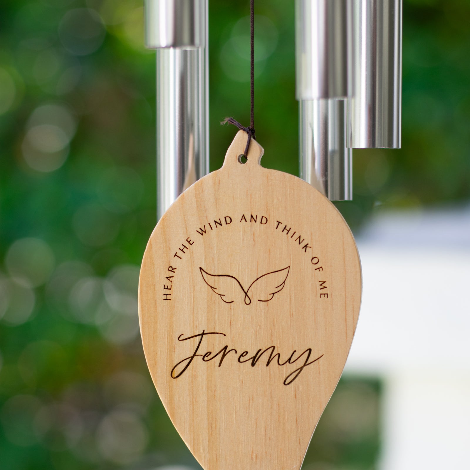 A close-up of a wooden leaf is at the bottom of a wind chime with the text Jeremy and Hear the wind and think of me and metal tubes hanging at the top