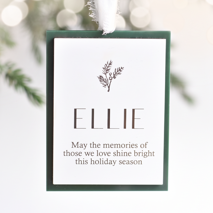 A personalized Christmas ornament tag with a white background, dark green border, and a white hanging ribbon. The tag is personalized with the name &
