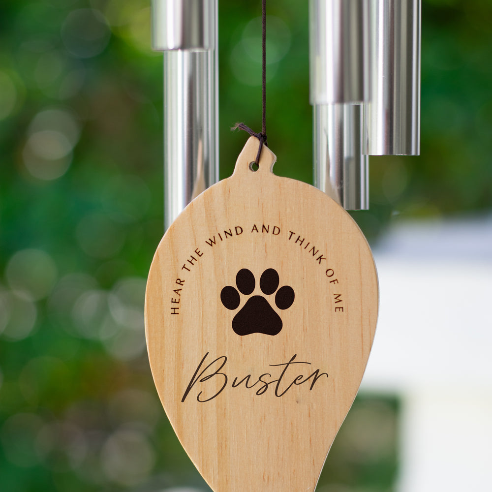 A close-up of a wooden leaf is at the bottom of a wind chime with a paw print and the text Buster and Hear the wind and think of me
