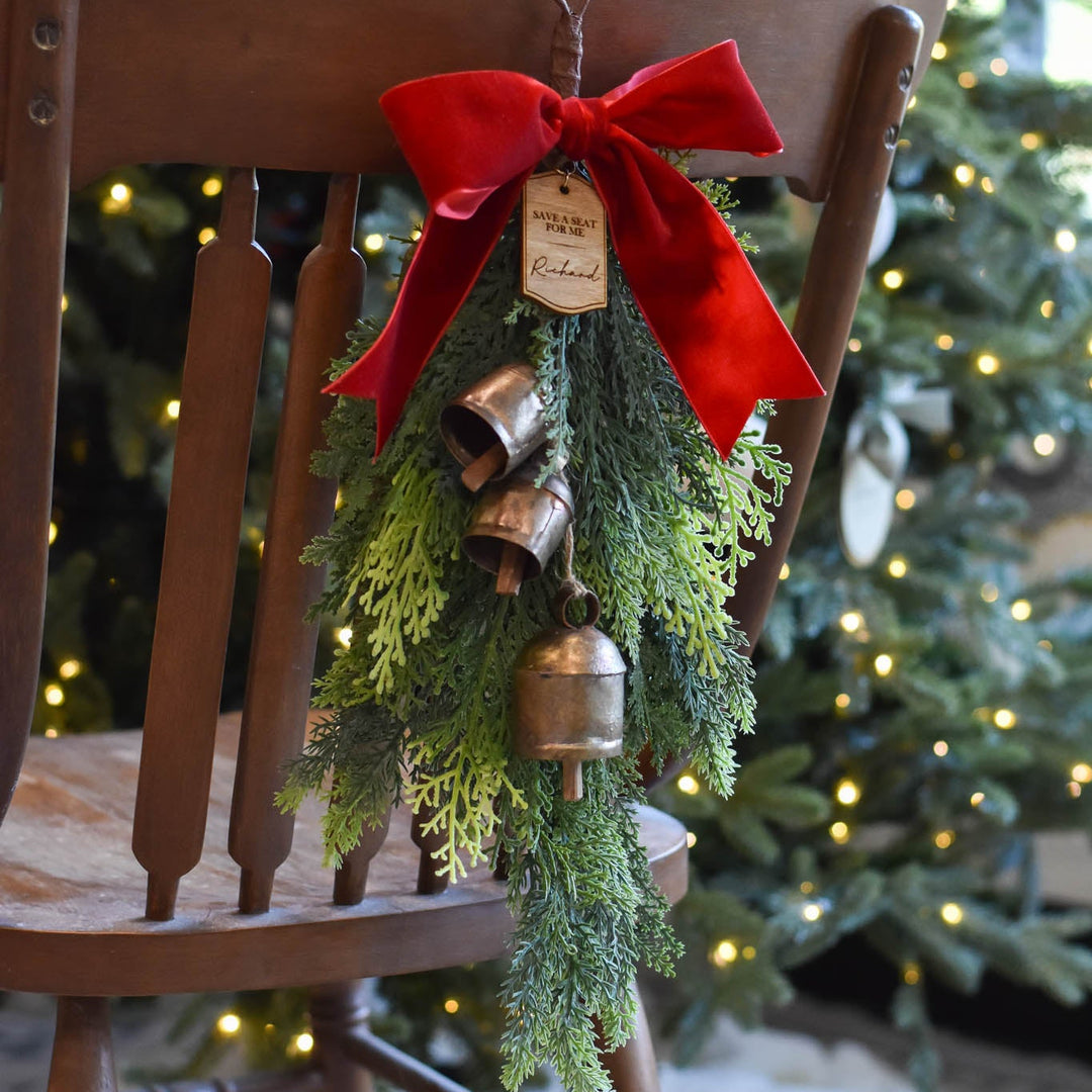 Save Me a Seat Holiday Swag featuring faux cedar greenery, vintage-style copper bells, and a red velvet bow.