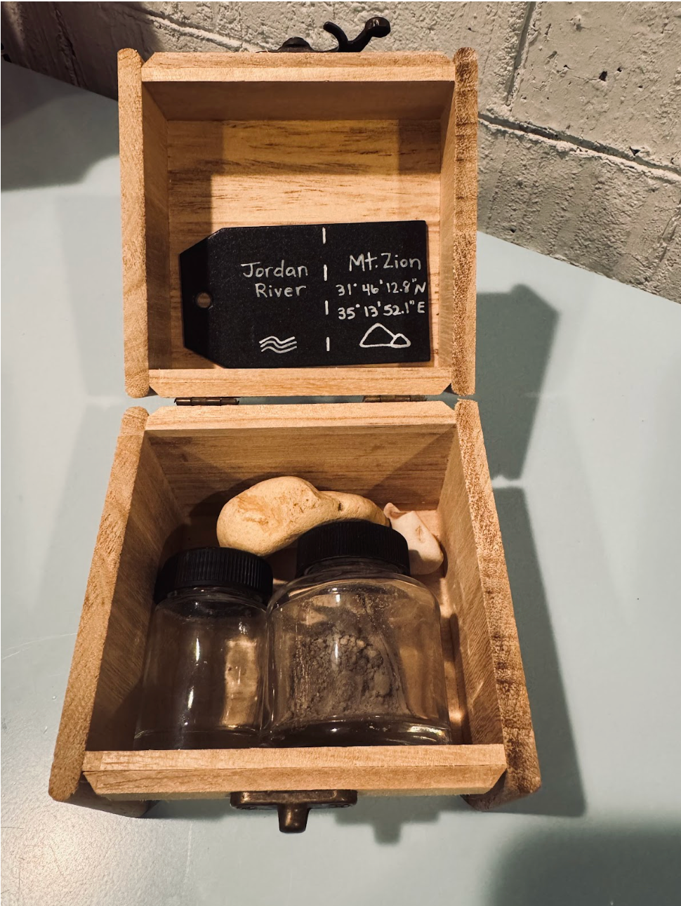 open wooden box with the words "Jordan River Mt. Zion" on the top of the bo and some jars and rocks in the bottom of the box