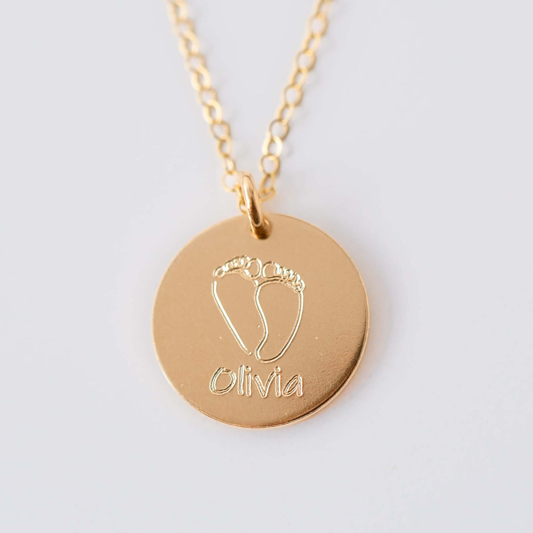 Baby Footprints Necklace in gold with engraved baby feet and the name 'Olivia' on a round charm.