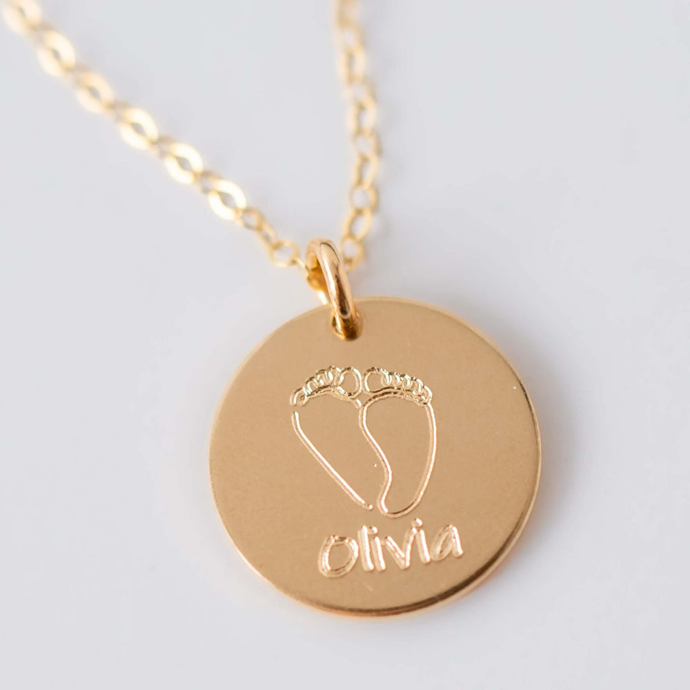 Baby Footprints Necklace in gold, round charm with engraved baby feet and the name 'Olivia' in script.