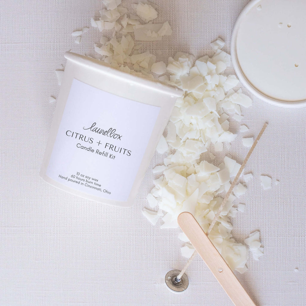 Candle Refill Kit, white container with label, soy wax flakes, wick clip, and wood stick on fabric background.