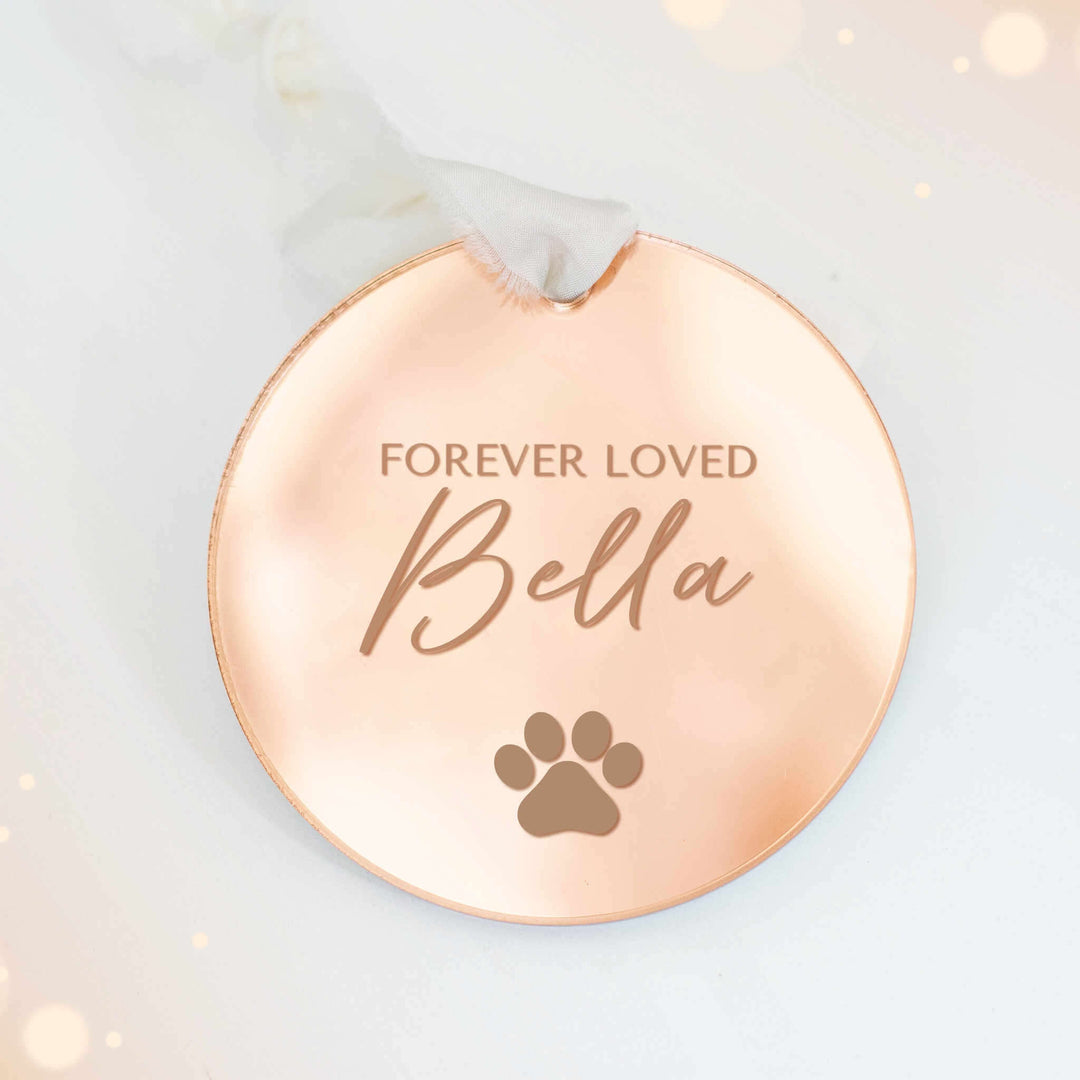 Custom Dog or Cat Memorial Ornament made of rose gold mirrored acrylic features the text 'Forever Loved Bella' and a paw print.