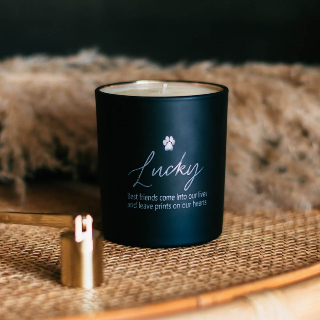 Custom Engraved Pet Memorial Candle in a matte black jar, engraved 'Lucky' and text, placed on a woven surface.