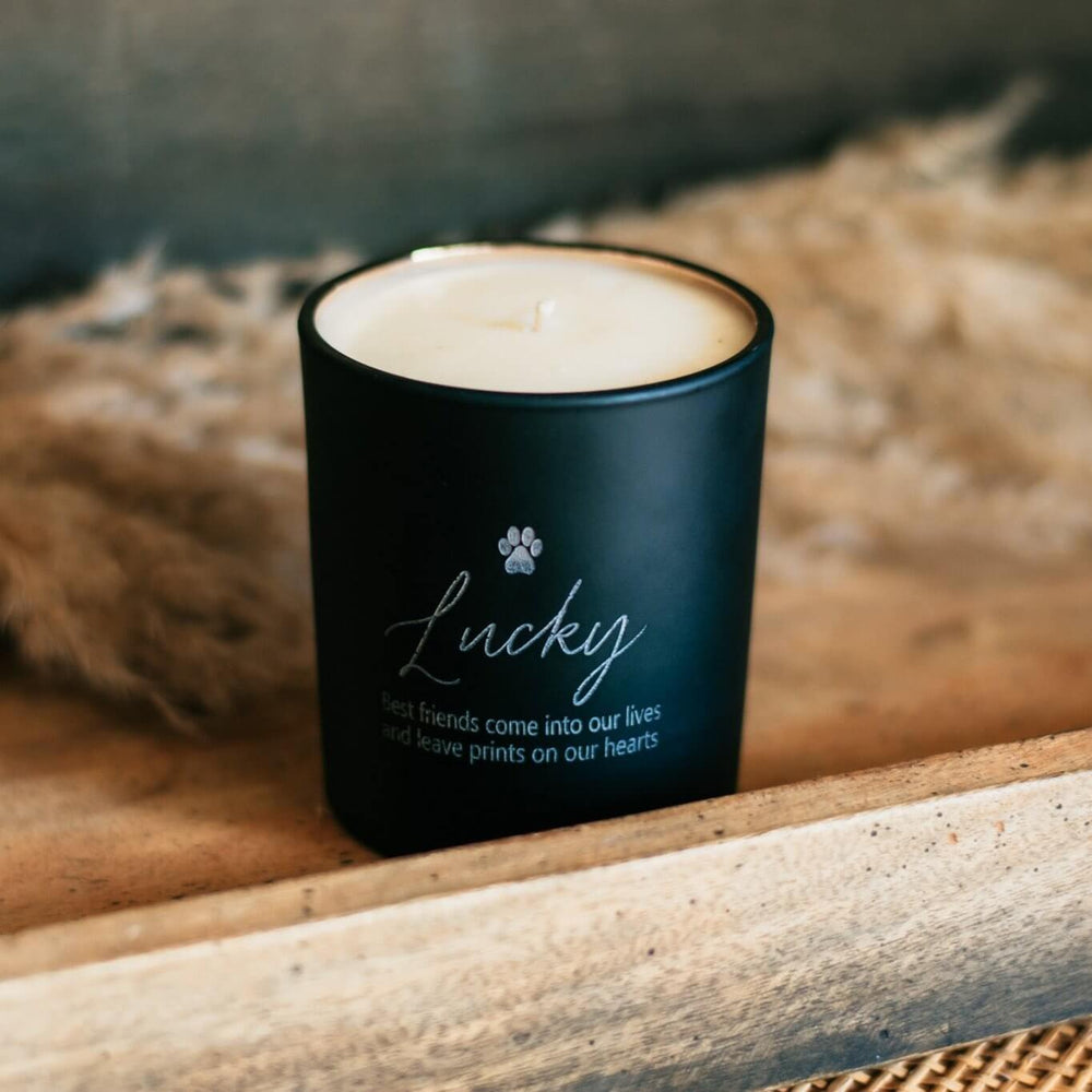 Custom Engraved Pet Memorial Candle in black glass, engraved with 'Lucky' and a paw print, placed on a wooden surface.