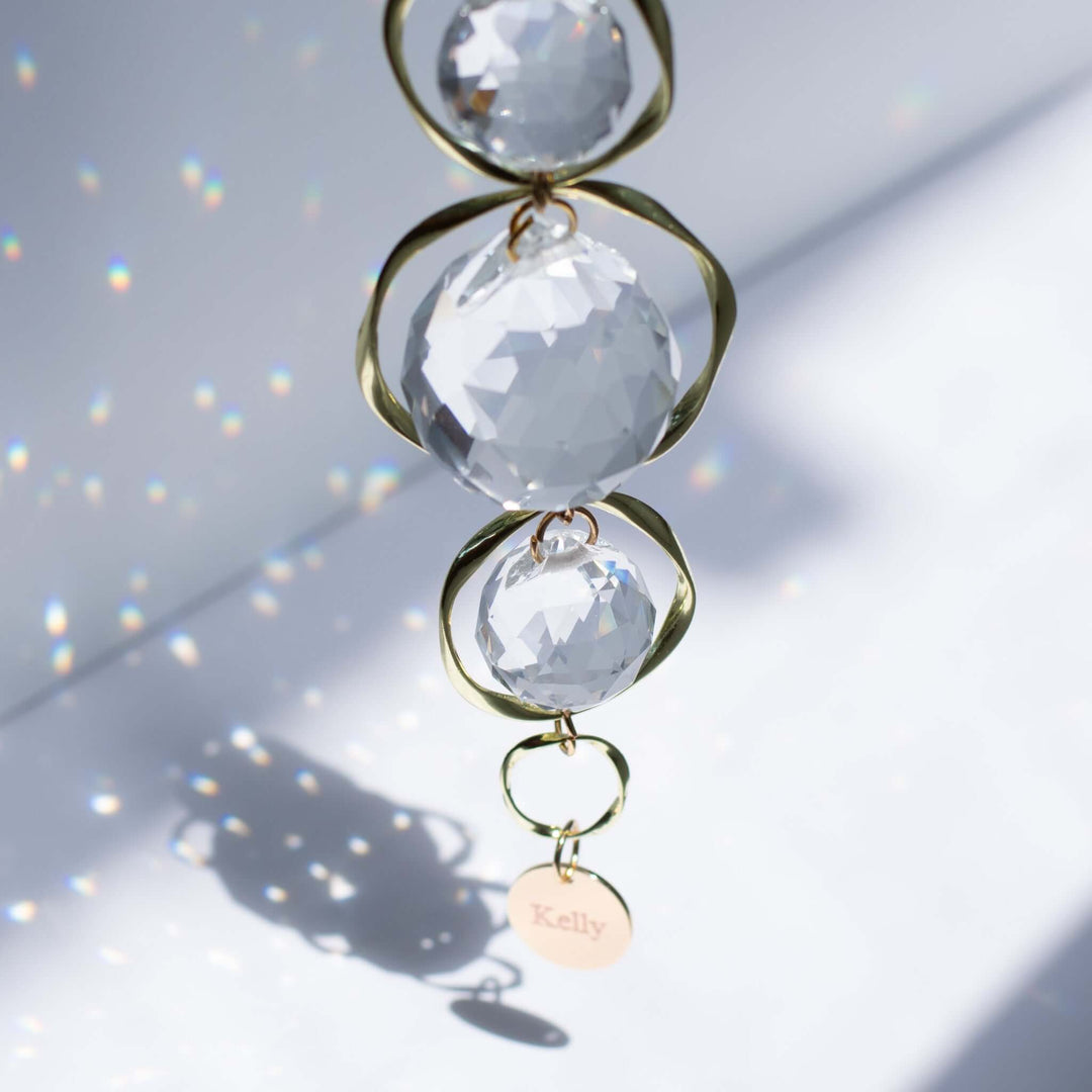 Custom Memorial Sun Catcher and Rainbow Maker features three crystal orbs with golden accents and a round engraved "Kelly" tag.