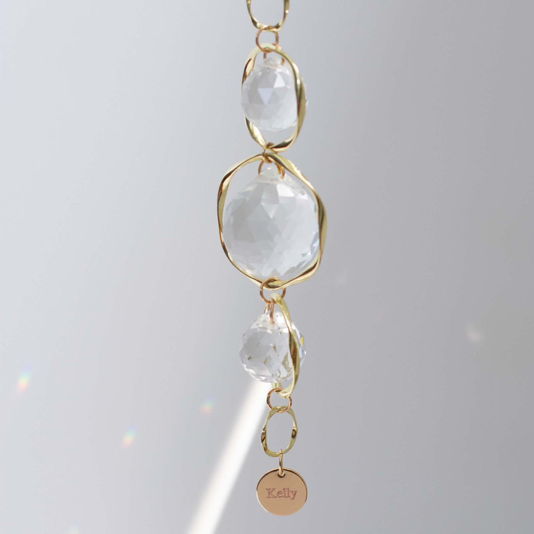 Custom Memorial Sun Catcher and Rainbow Maker with clear glass crystals and a gold frame, engraved charm reading 'Kelly'.