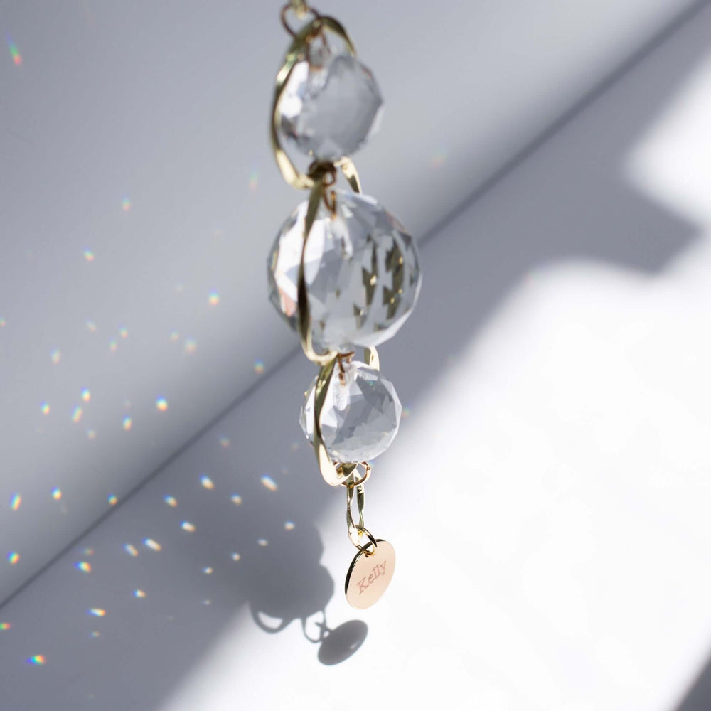 Custom Memorial Sun Catcher and Rainbow Maker featuring clear crystal orbs and a gold chain with a round engraved charm.