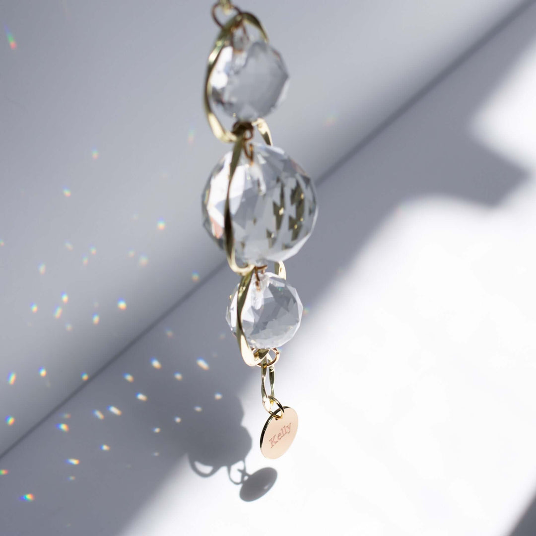 Custom Memorial Sun Catcher and Rainbow Maker featuring clear crystal orbs and a gold chain with a round engraved charm.