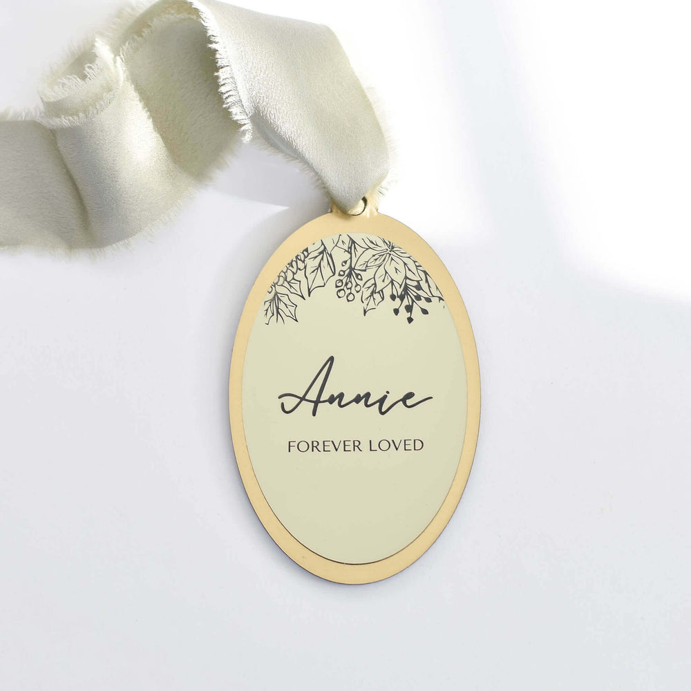 Forever Loved Ornament, oval gold and cream acrylic, engraved 'Annie', attached with light gray ribbon.