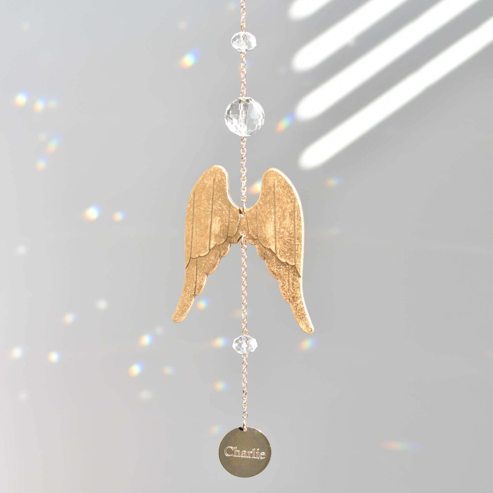 Light of an Angel golden angel wing sun catcher with crystal beads and engraved disc hanging against grey background.