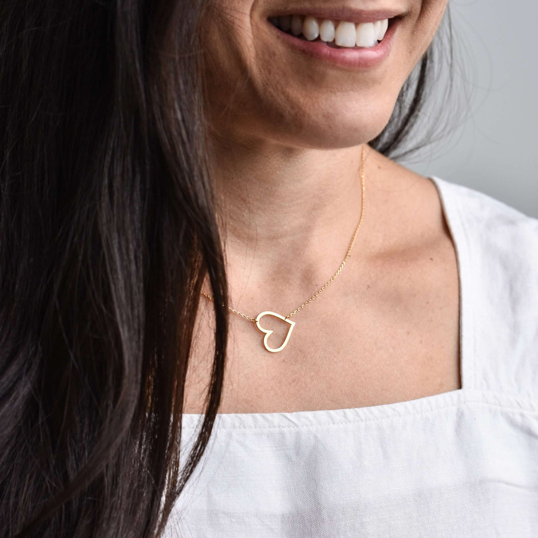 Heart to Heart Necklace in gold, featuring an open heart design, worn on a person with dark hair and a white top.
