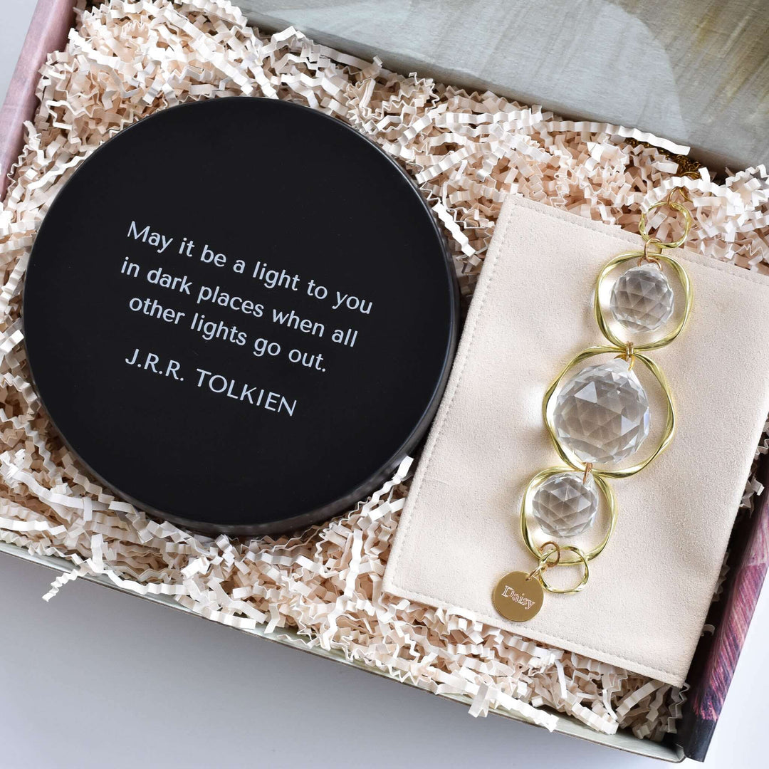 Light in Dark Places Gift Box includes a black round dish with engraved text and a cream pouch holding a crystal ornament.