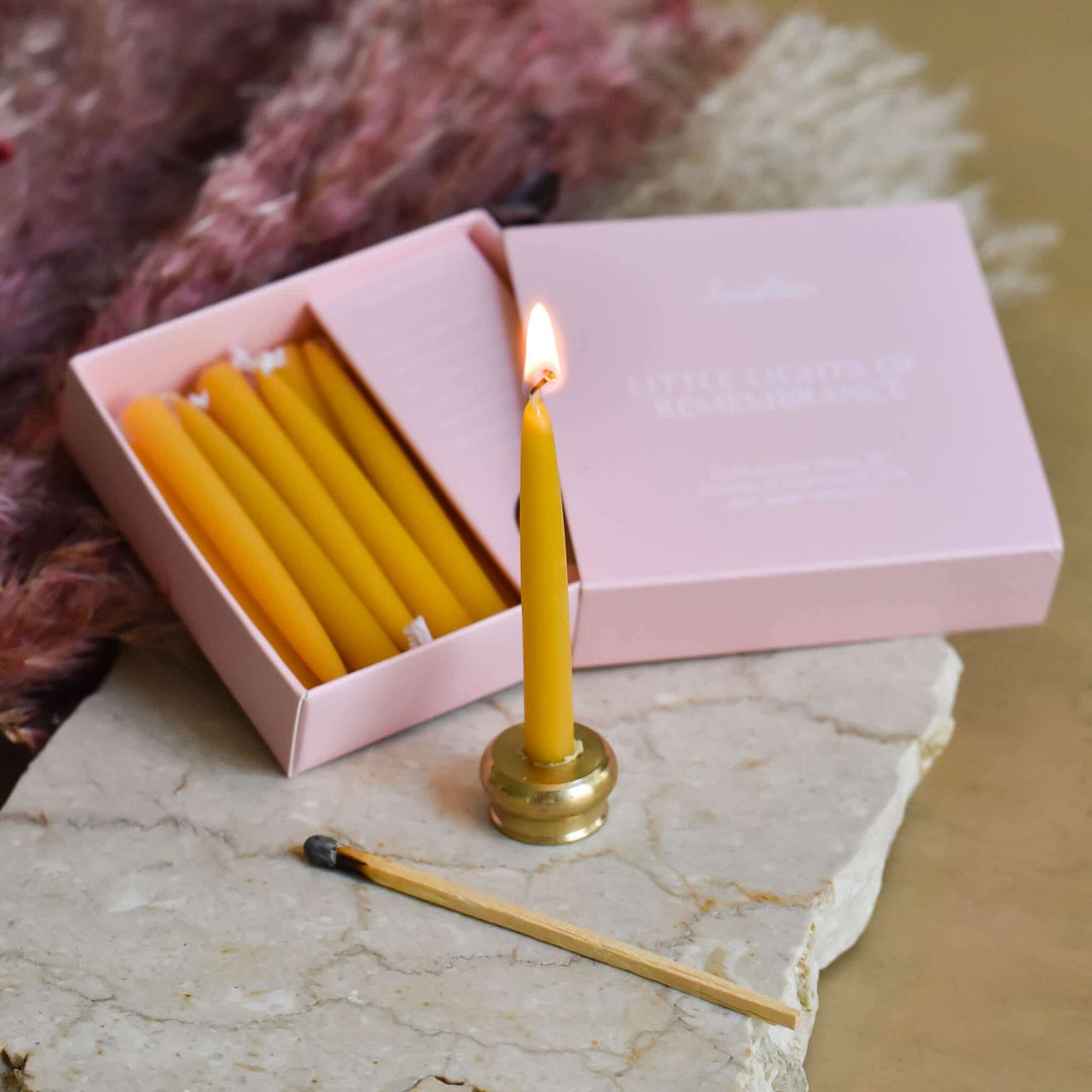 Little Lights of Remembrance box with yellow candles, one lit, resting on a marble surface with a match.