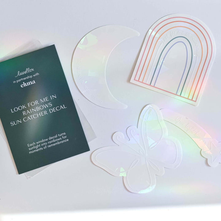 Four prismatic decals including a butterfly, moon, rainbow, and shooting star on a white surface. Look for me in Rainbows Sun Catcher Decal Set.