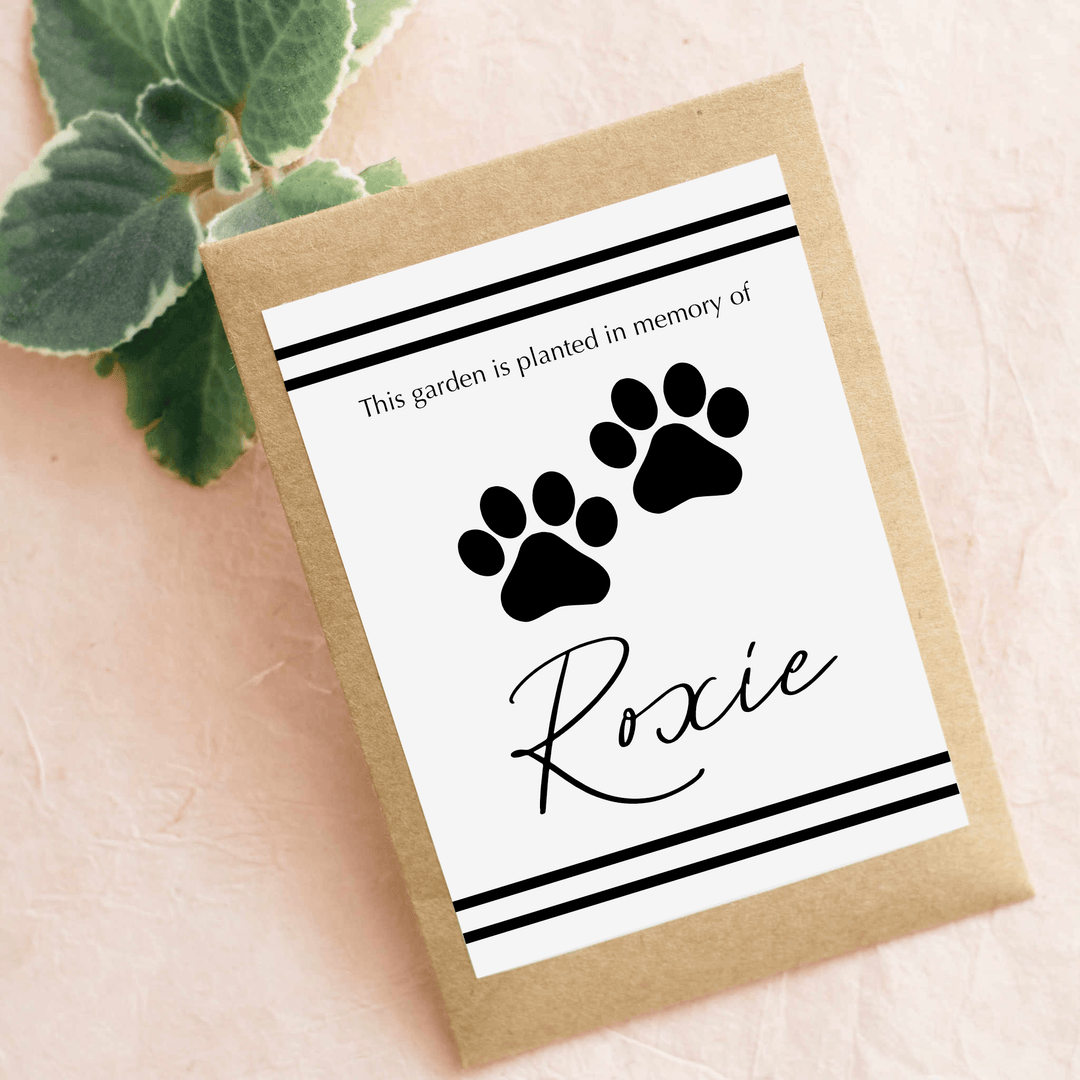In Memory of a Beloved Pet Garden Seed packet with black paw prints, a name "Roxie" in cursive, on a brown kraft background.
