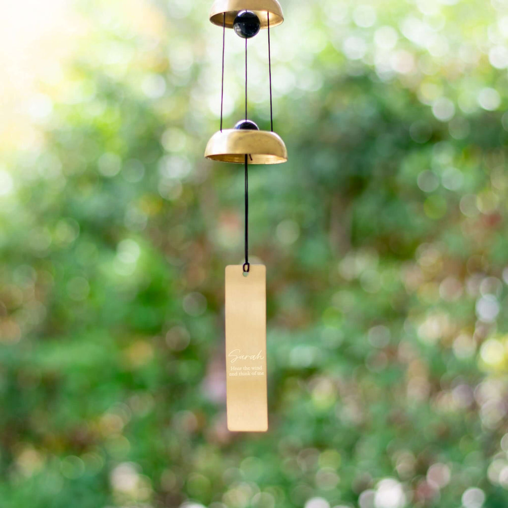 Memorial Wind Chime with two gold bells and a rectangular brass tag engraved with the name Sarah, hanging in a garden.