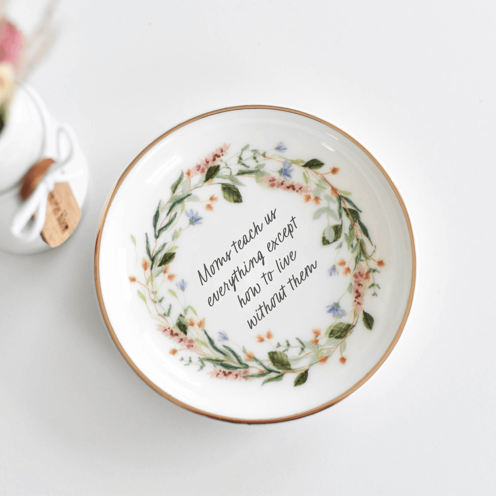 A Mom's Love Jewelry Dish, round porcelain dish with floral design, gold rim, black text reads: 'Moms teach us everything except how to live without them.'