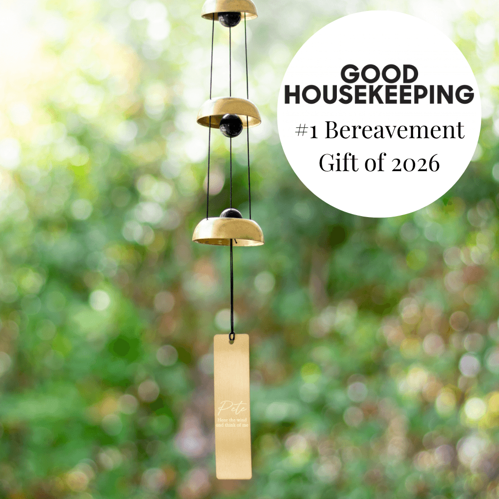 Memorial Wind Chime made of gold-toned metal with three bells and engraved name tag on a blurred natural background.