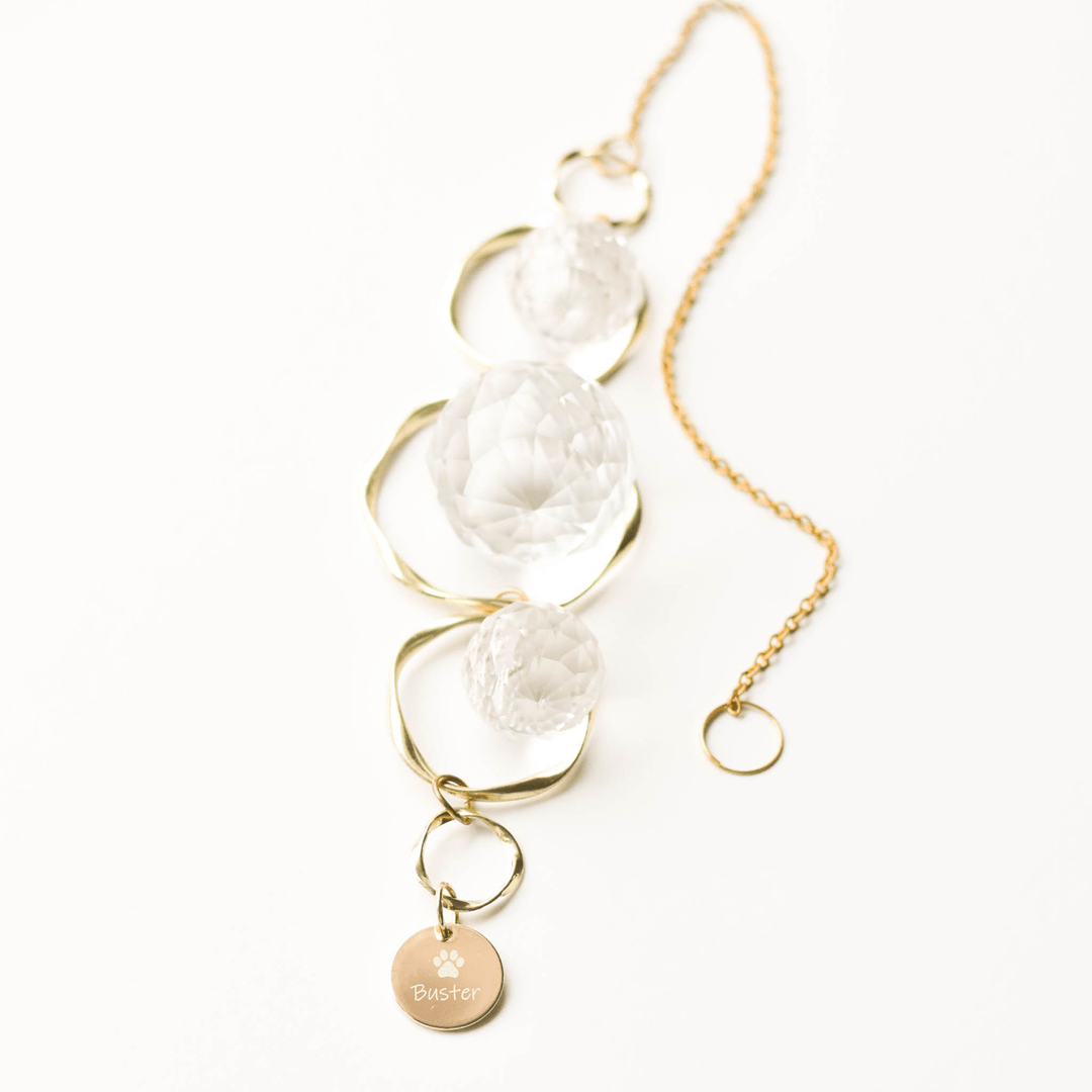 Pet Memorial Sun Catcher and Rainbow Maker with clear glass orbs and gold chain, engraved "Buster" with paw print charm.