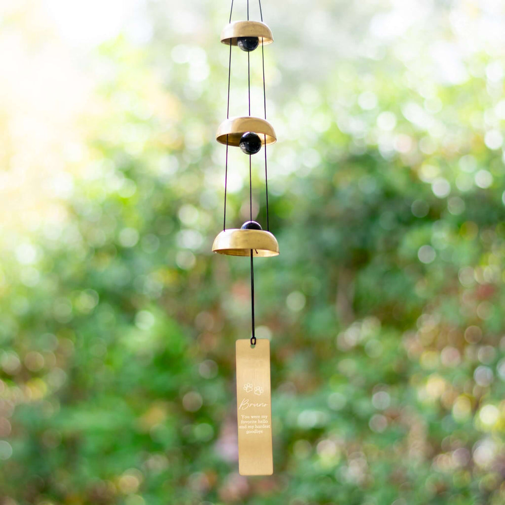 Pet Memorial Wind Chime with three gold metal bells and a gold engraved tag, suspended against a blurred green background.