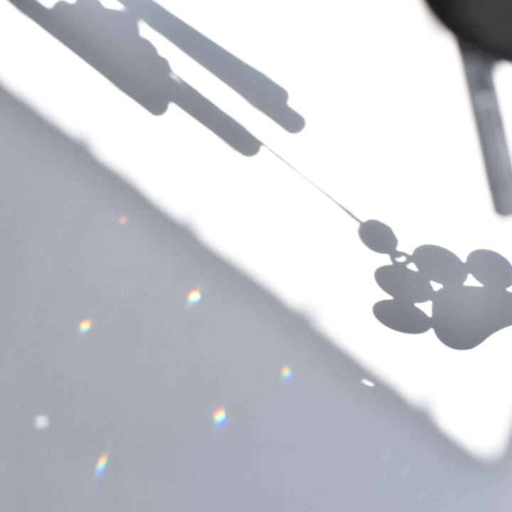 Shadow of a Rainbow Bridge Dog Wind Chime with a paw print design, casting colorful light reflections on a surface.