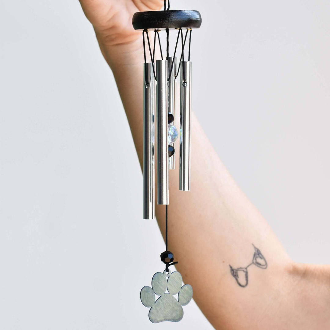 Rainbow Bridge Dog Wind Chime with silver tubes, a paw print charm, and crystal detail held by a hand.