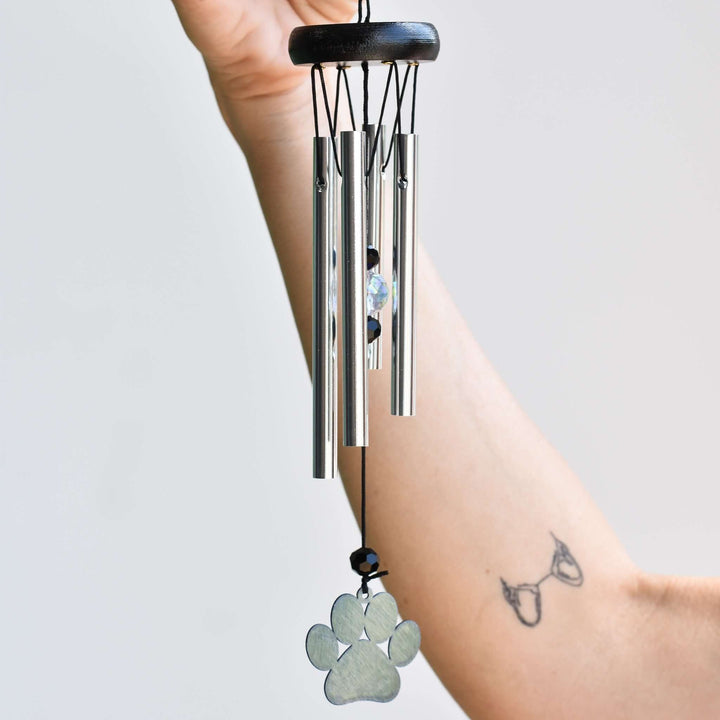 Rainbow Bridge Dog Wind Chime with silver tubes, a paw print charm, and crystal detail held by a hand.