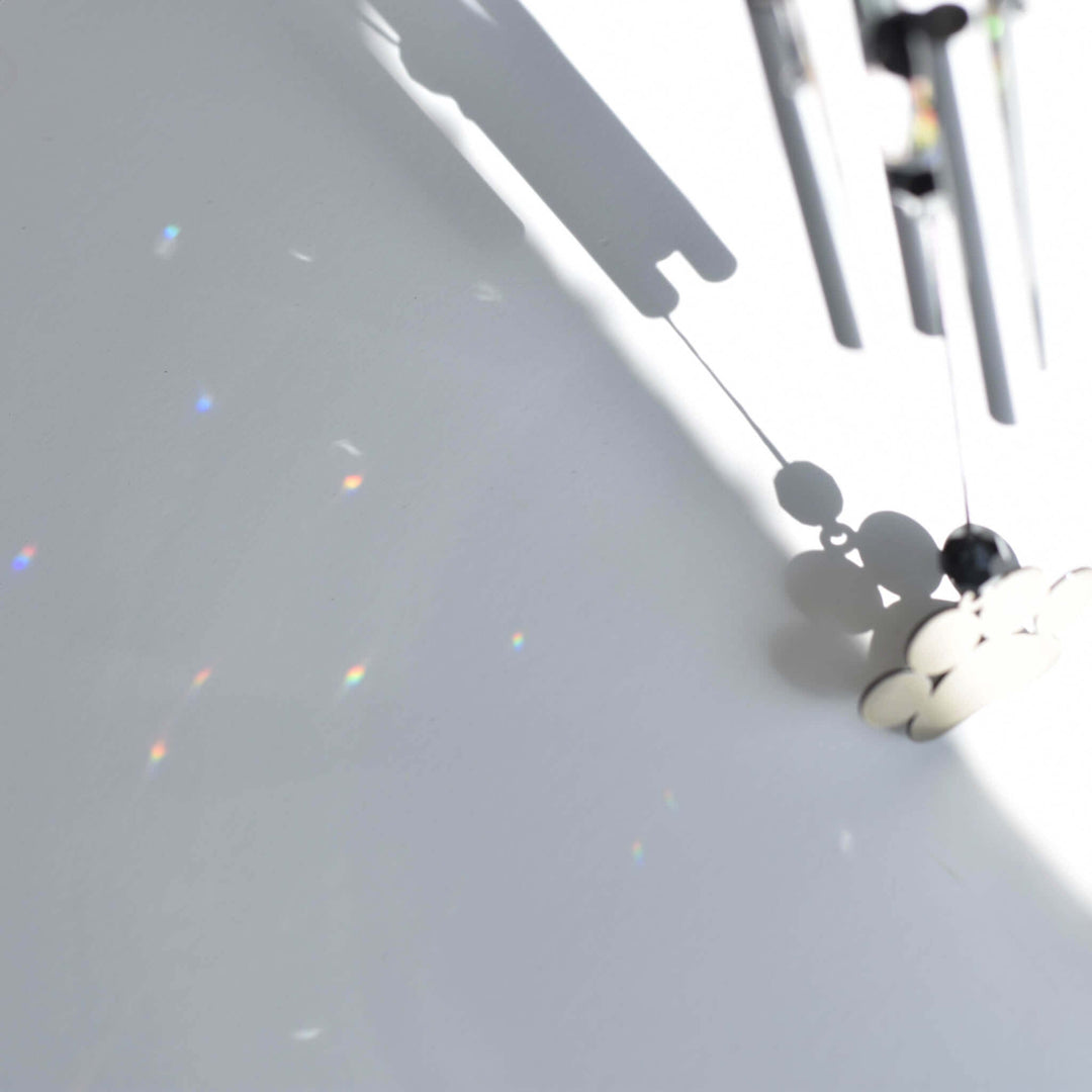 Rainbow Bridge Dog Wind Chime showing silver chimes and colorful light reflections on a white surface.