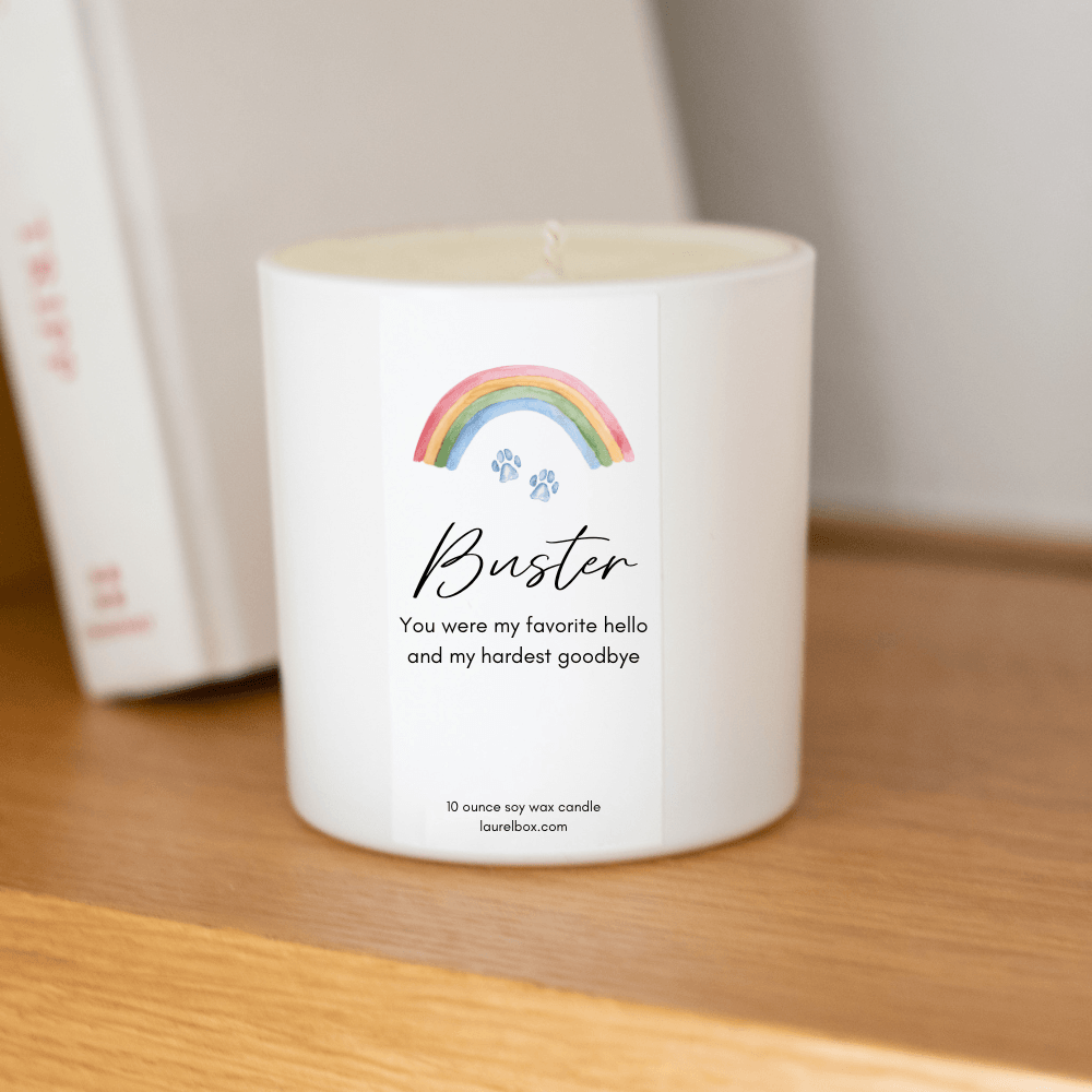 Rainbow Bridge Pet Memorial Box white candle with rainbow design and personalized label for Buster on a wooden shelf.