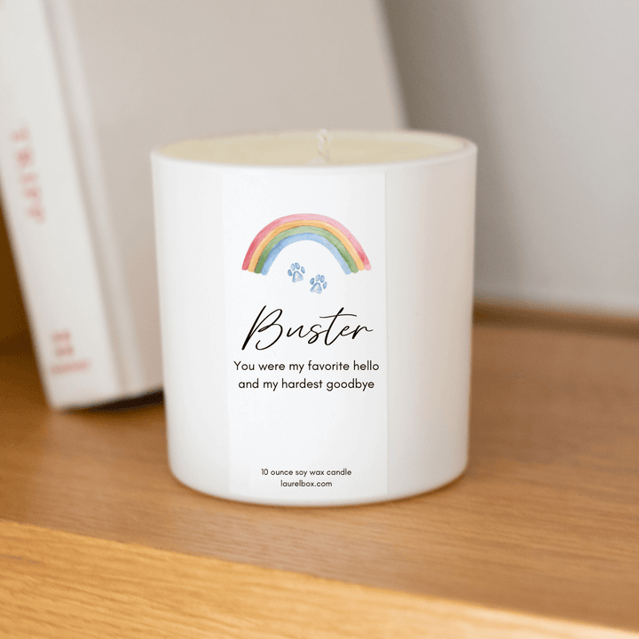 Rainbow Bridge Pet Memorial Box white candle with rainbow design and personalized label for Buster on a wooden shelf.