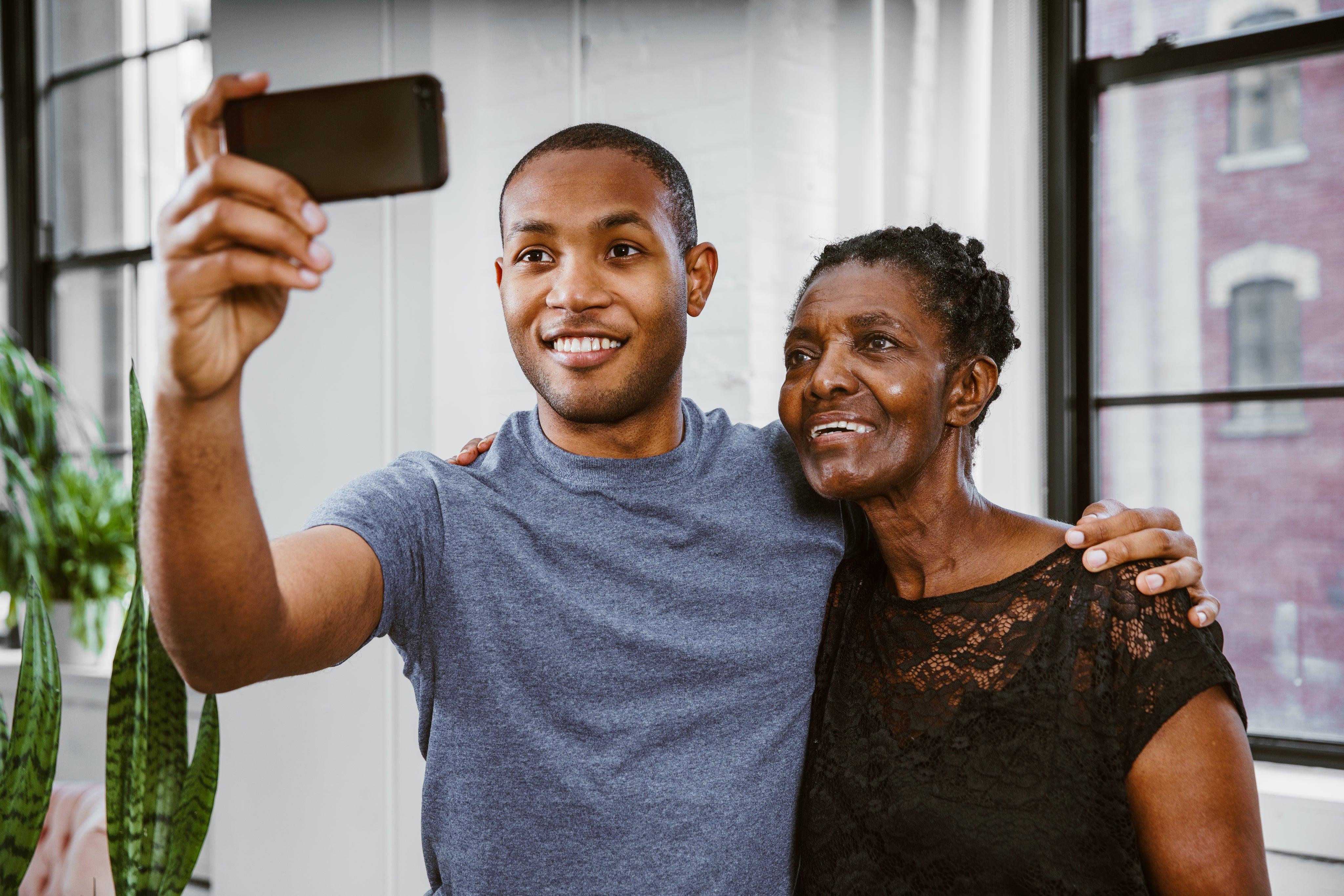 photo of a young man with his hand around an older woman’s shoulder taking a picture of the both of them