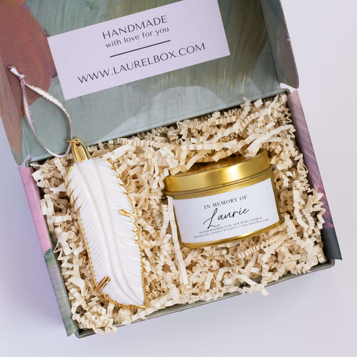 Morningside Resident Sympathy Gift box with a white feather ornament and gold-scented candle, all in shredded paper.