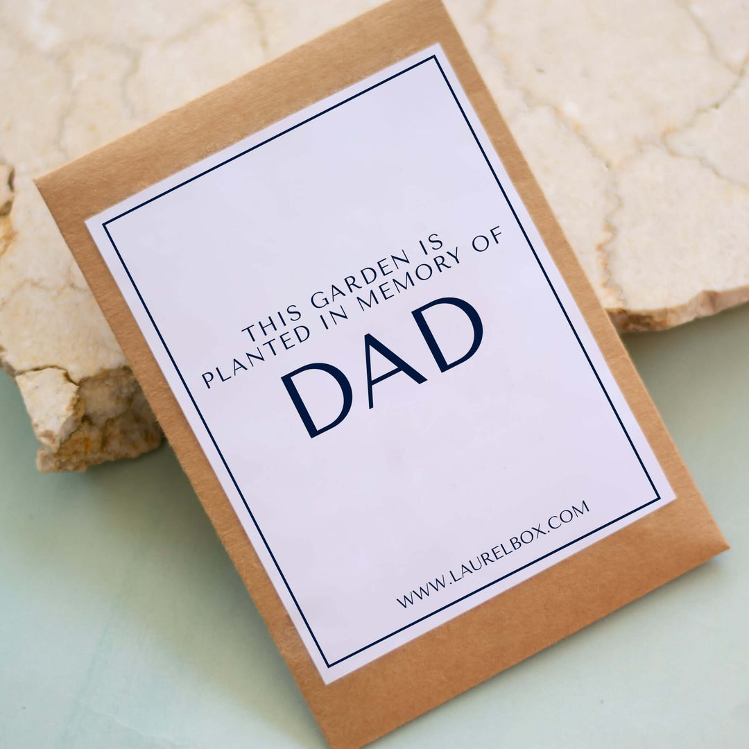 In Memory of Dad Garden Seed packet on a light green surface with a cream stone backdrop, featuring text about the garden.