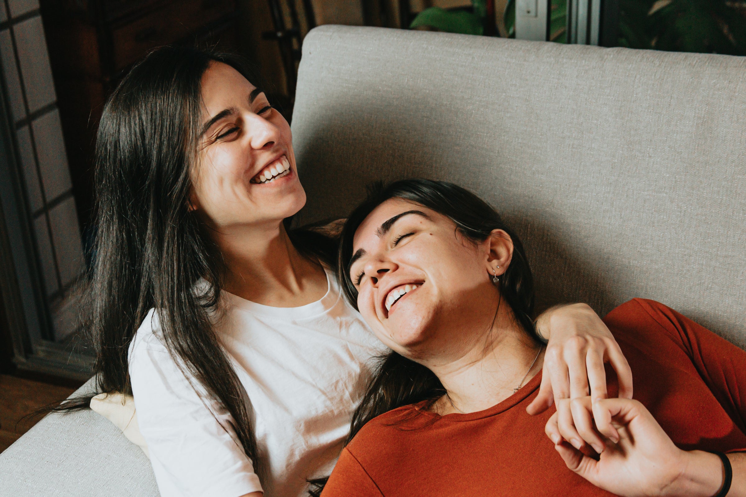 two women sitting on a couch smiling and laughing