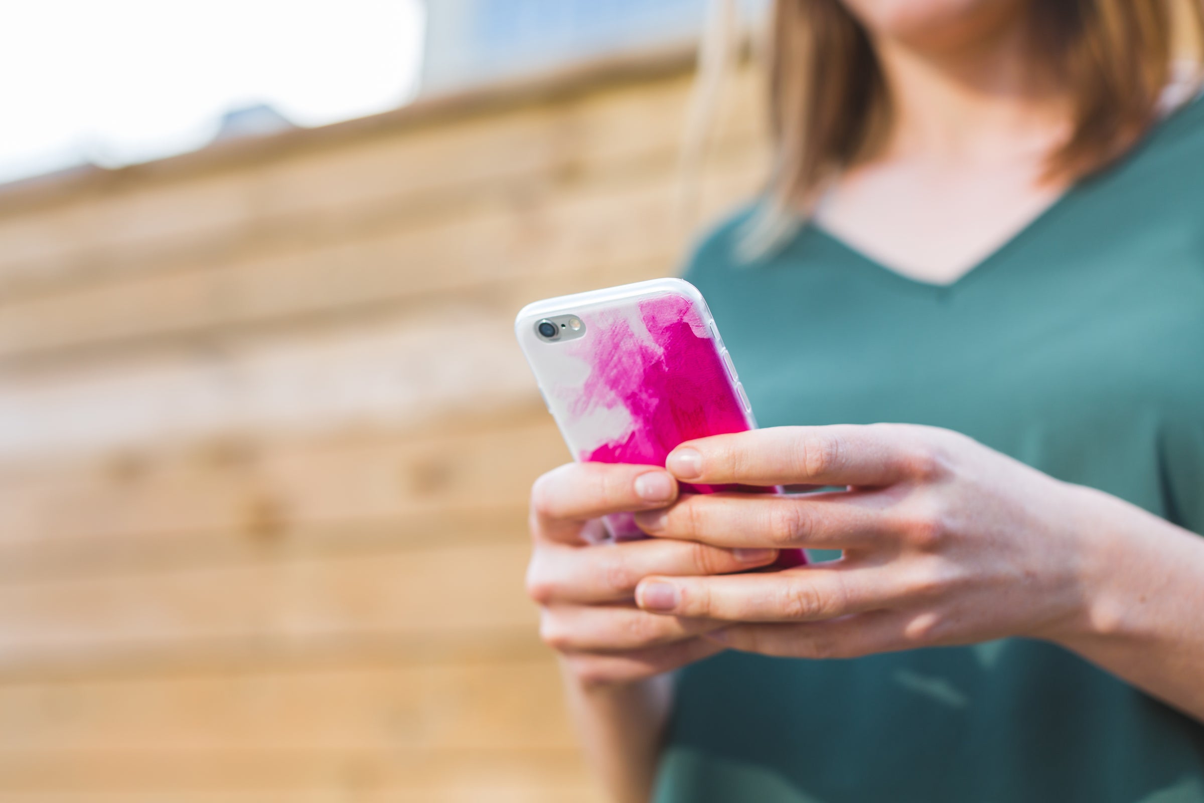young woman in a green t-shirt holding a phone in a pink phone case 