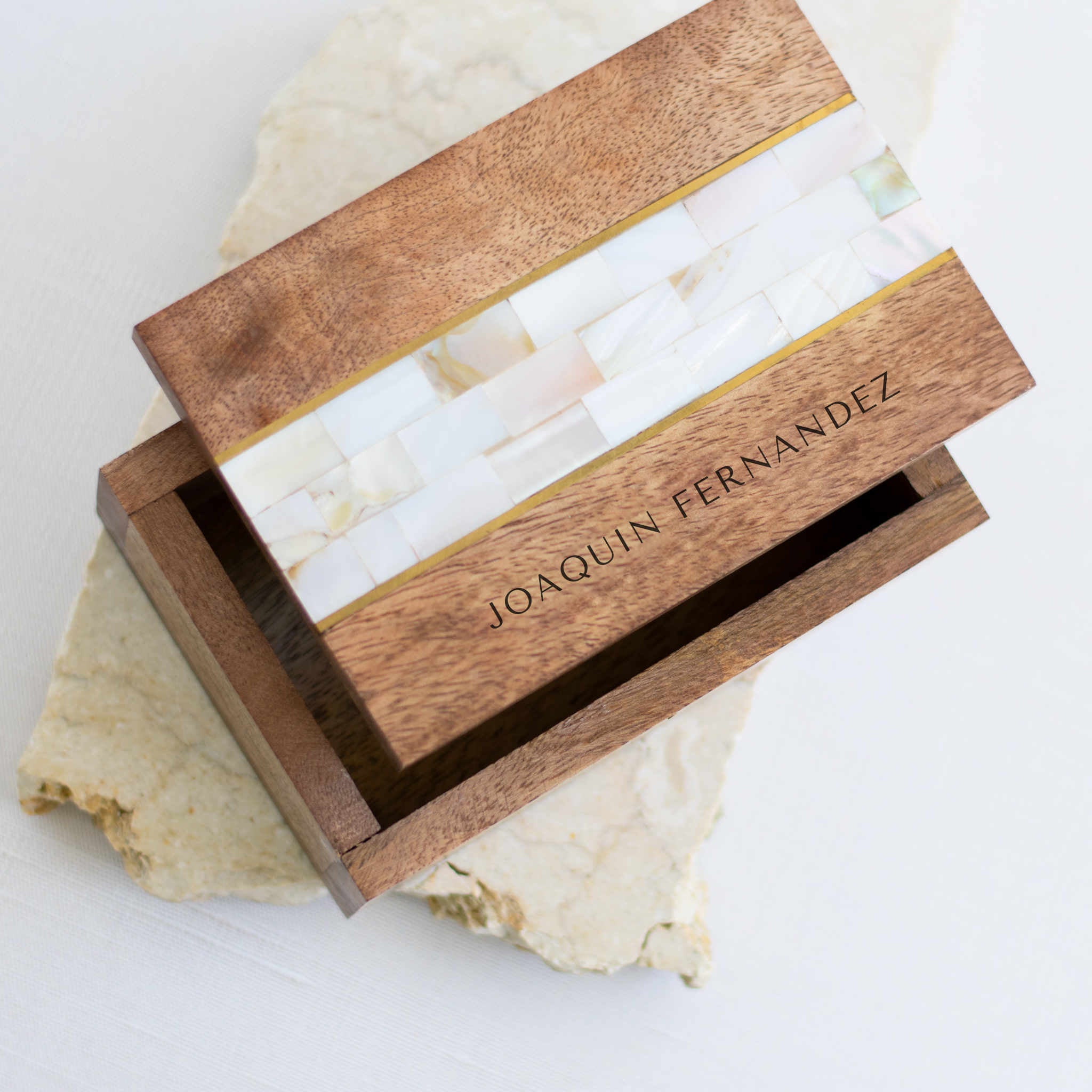 A close-up of an opened wooden memory box with mother-of-pearl stones in the middle, with an engraved Joaquin Fernandez text at the bottom, and placed on top of a granite surface.