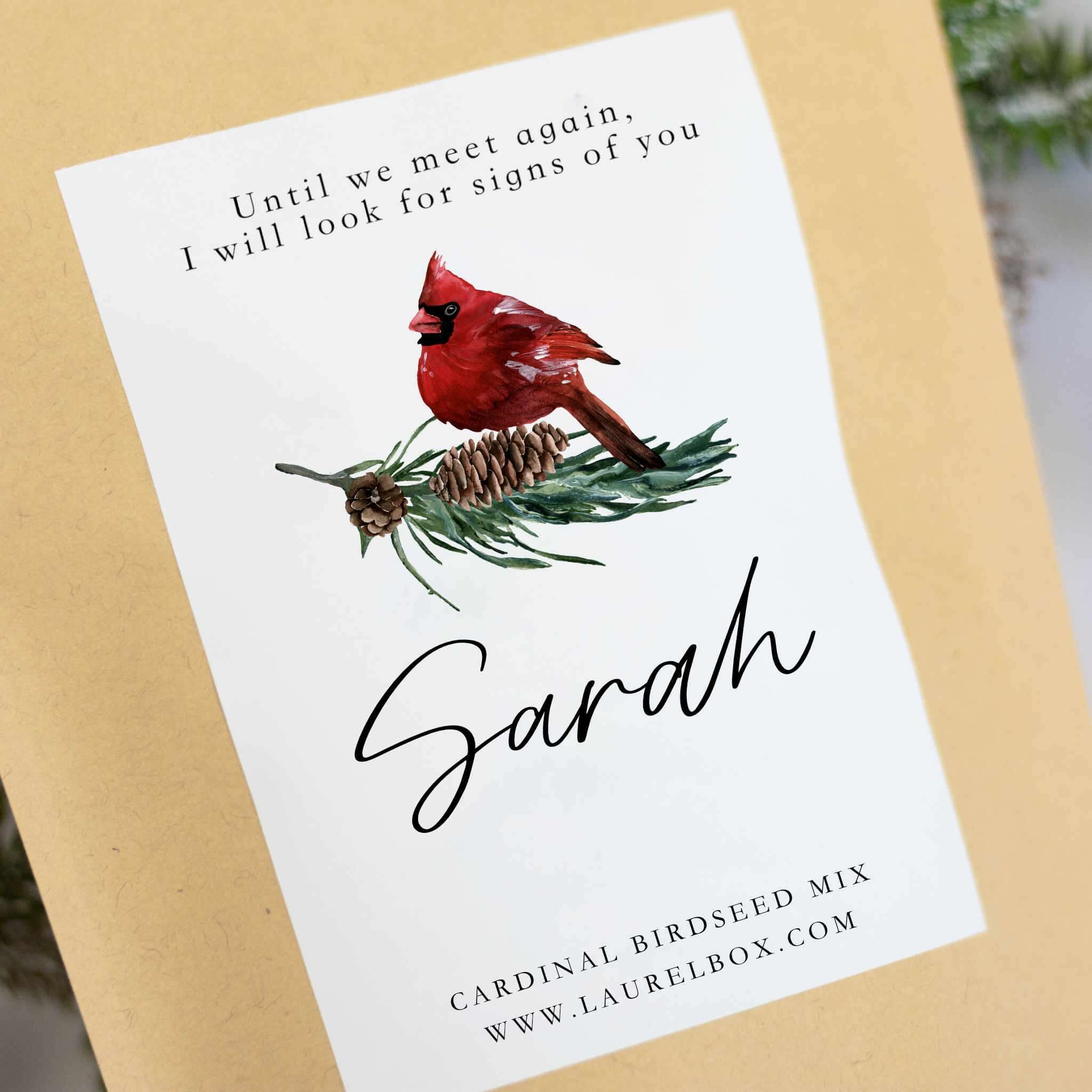 Cardinal bird on pine branch with pine cone; text includes 'Until we meet again' and name 'Sarah'; custom birdseed mix.