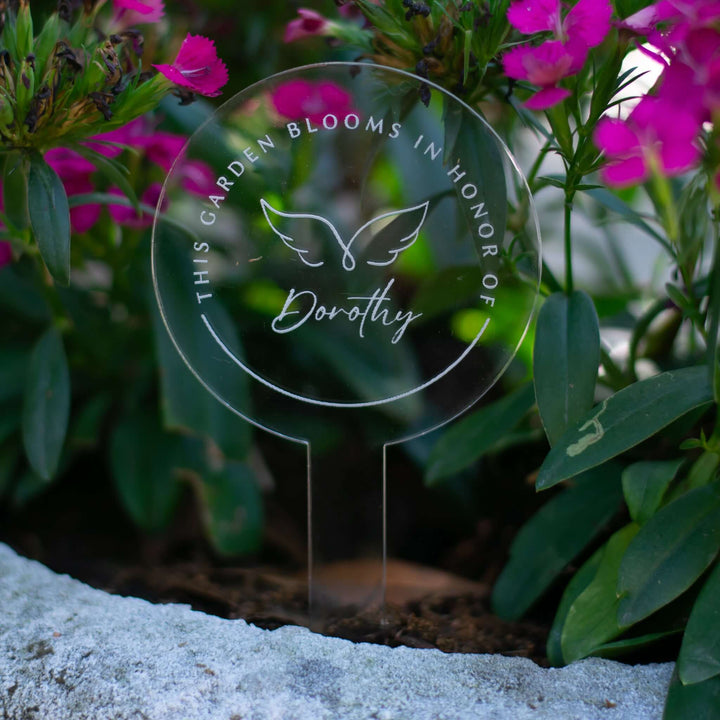 Custom Memorial Garden Stake made of clear acrylic, engraved with "This Garden Blooms in Honor of Dorothy," set among flowers.