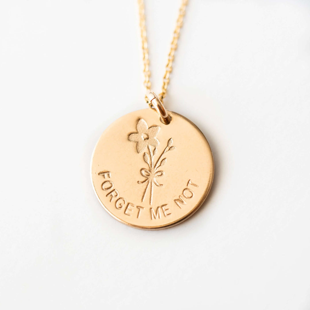 Forget Me Not Necklace in gold with an engraved flower design and text, on a delicate chain.