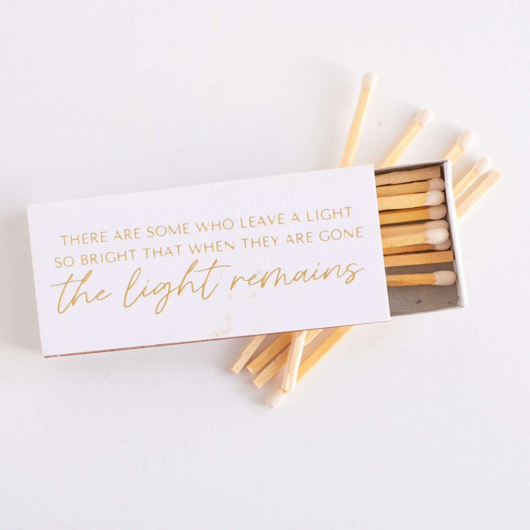 Remembrance matchbox with text, gold font on white, wooden matches visible, part of condolence gift for Their Light Remains.