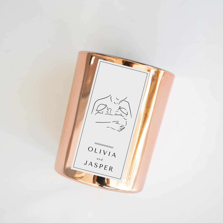 Twin Loss Memorial Candle in a rose gold container, featuring a label with illustrations of two babies and names Olivia and Jasper.