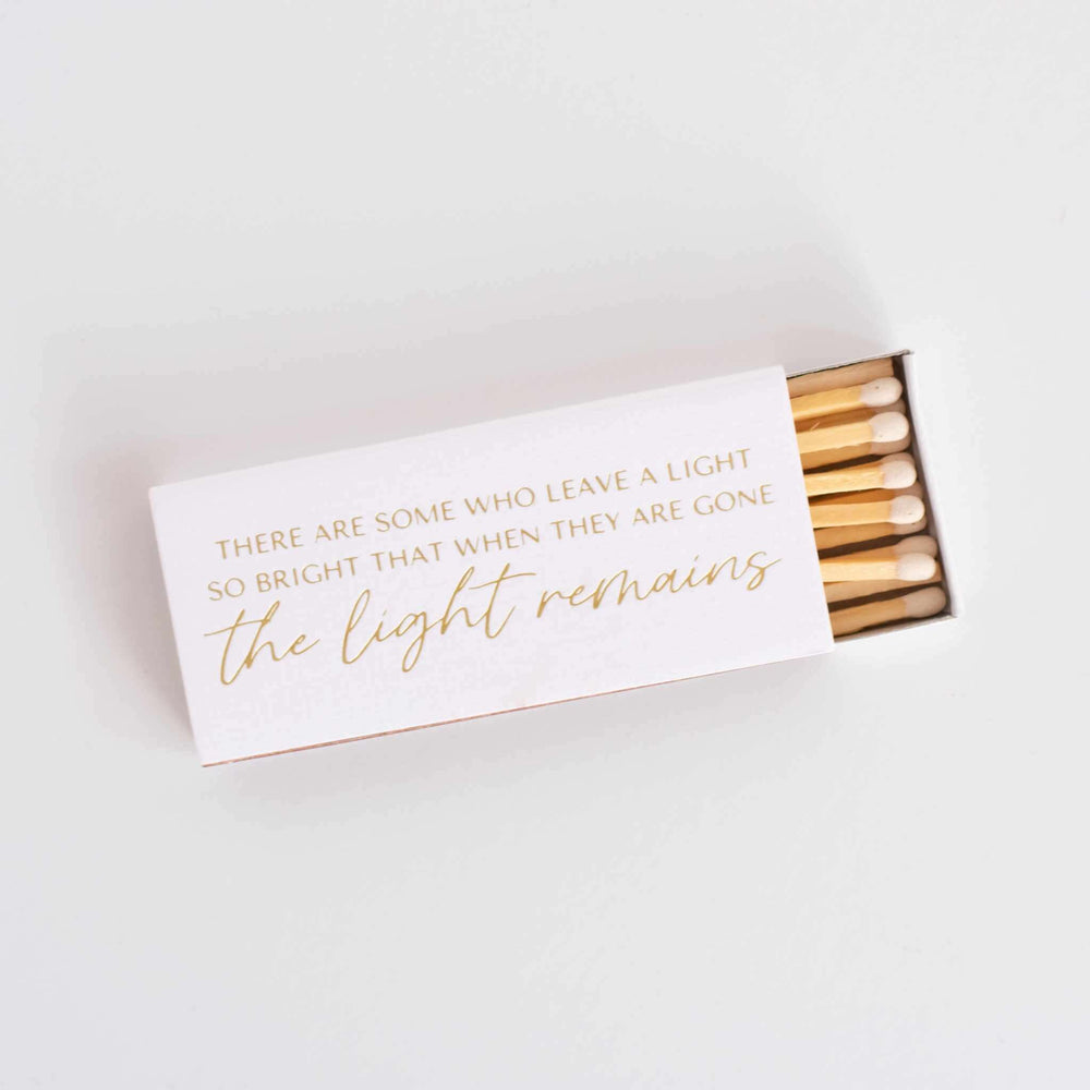 White linen matchbox with gold foil text, contains wooden matches. Text reads "There are some who leave a light...the light remains." Their Light Remains Matches.